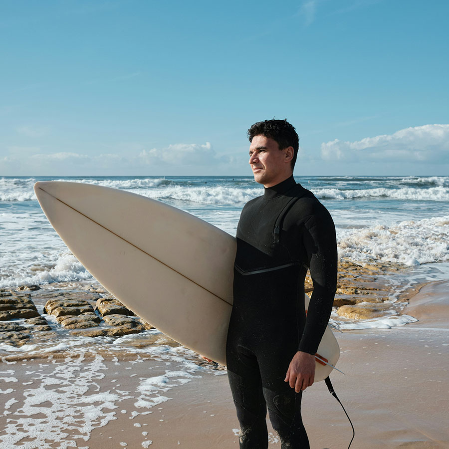 Person in wetsuit standing with surf board on sandy coastal beach.