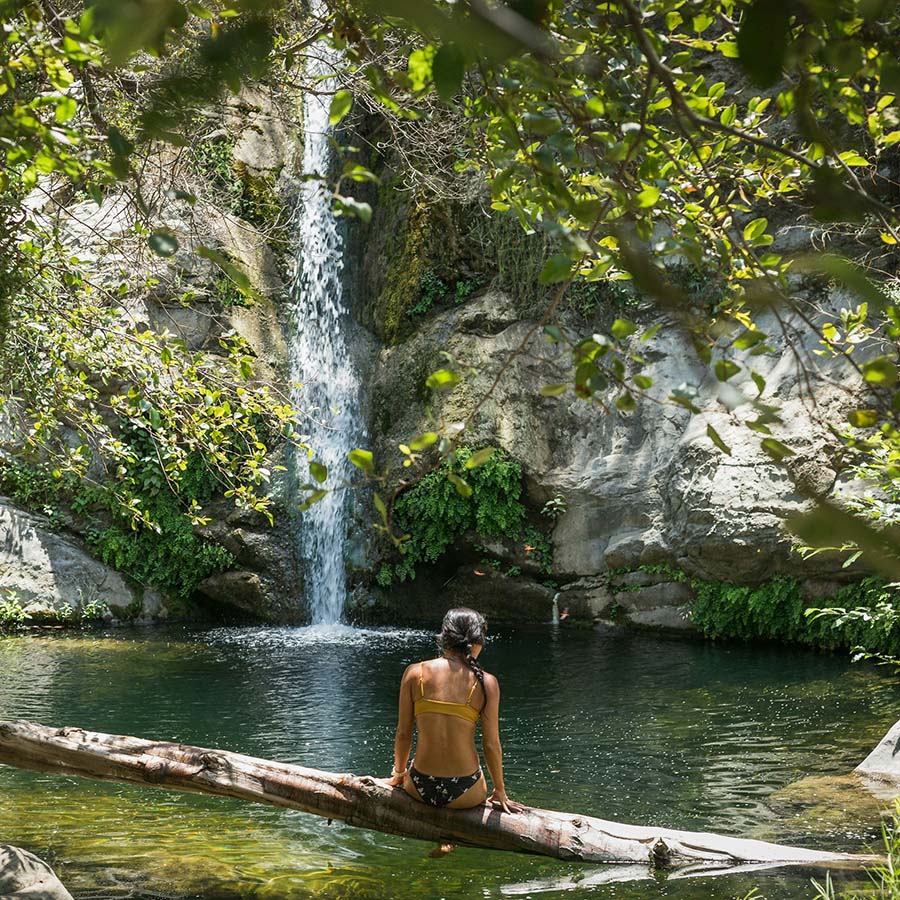 Person sitting on fallen tree in front of tranquil waterfall.