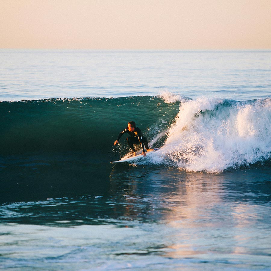 Person surfing wave at sunset.