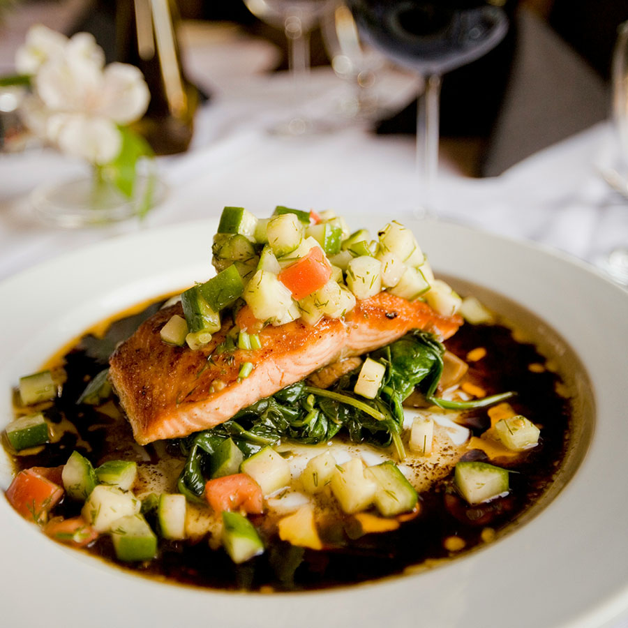Elegantly plated fish dish with glass of wine on white tablecloth.