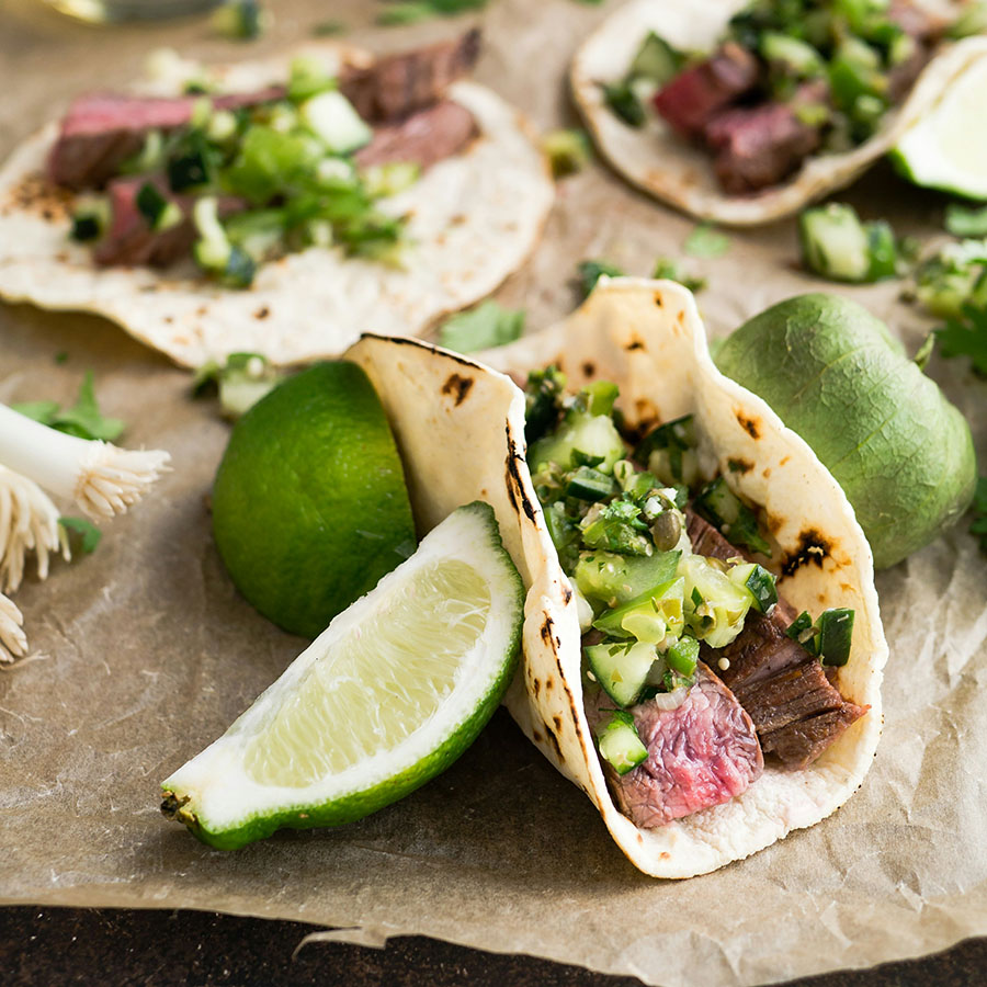 Street tacos with meat, vegetables, and limes on dining table.