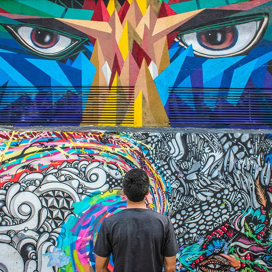 Person looking at mural with geometric shapes and large eyes.