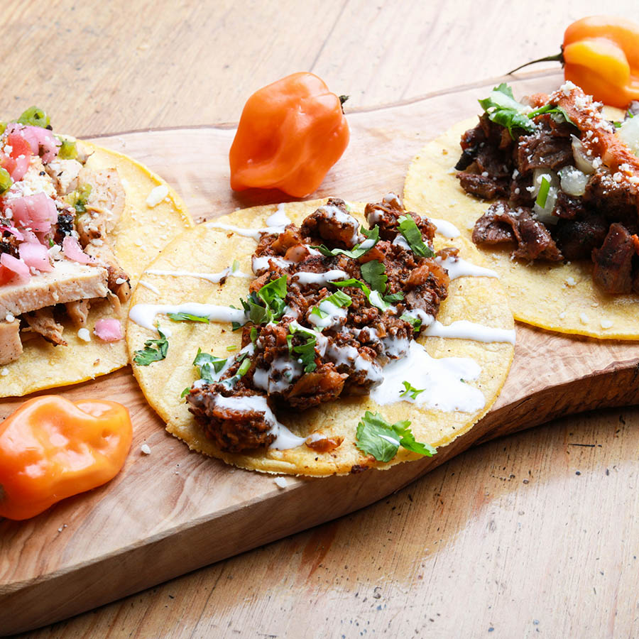Platter of street tacos and spicy peppers on table.