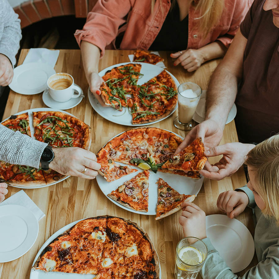 Family eating pizzas together at large dining table.