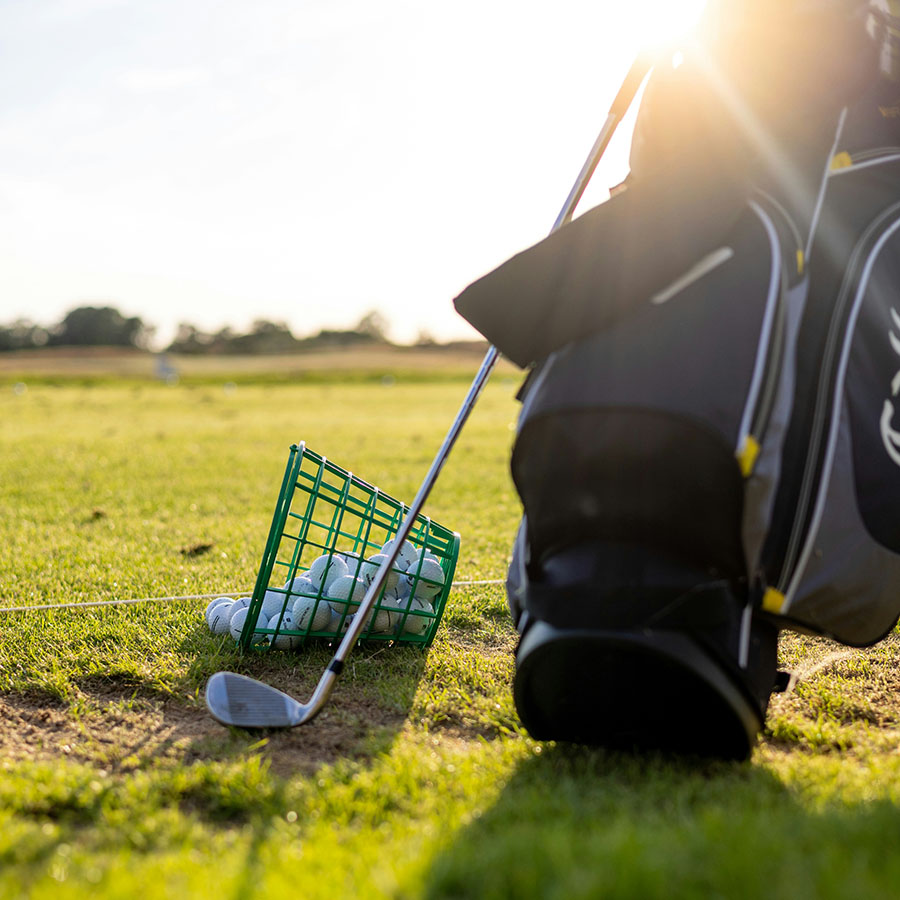 Golf bag, clubs, and bucket of golf balls on golf course in the sunshine.