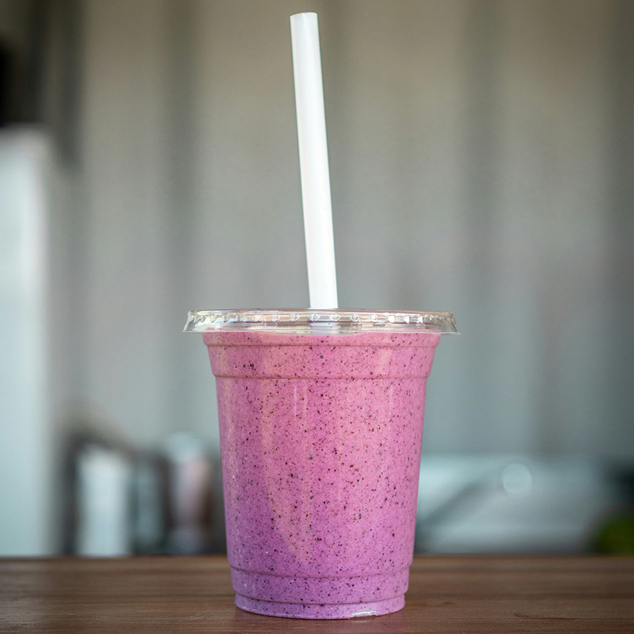 Purple fruit smoothie in plastic cup with long straw.