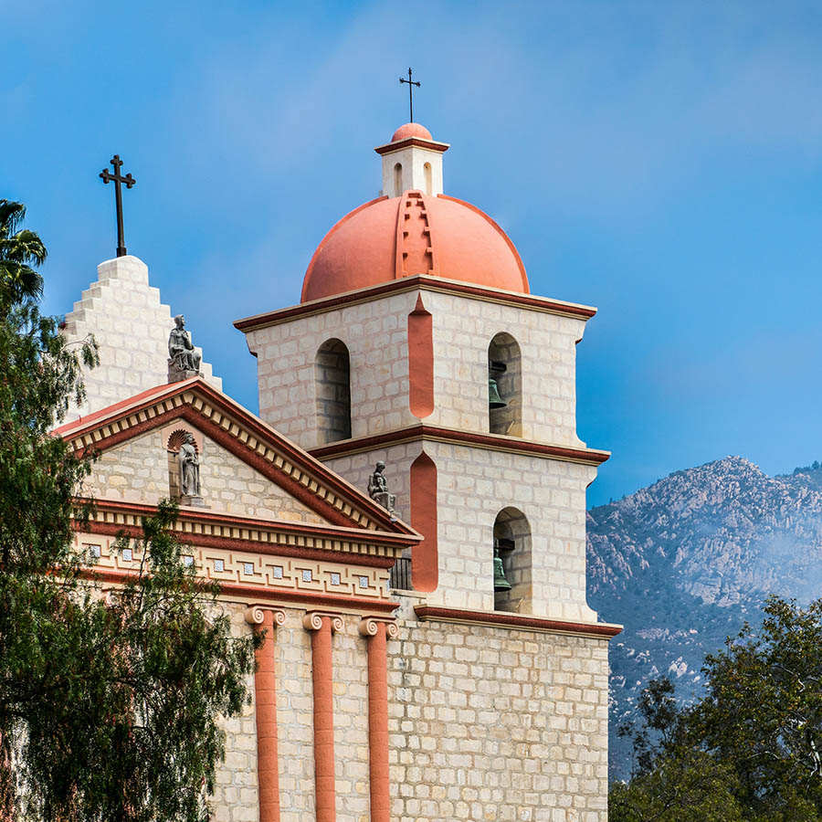 Stone tower of the Santa Barbara Mission with distant rocky mountaintops behind.