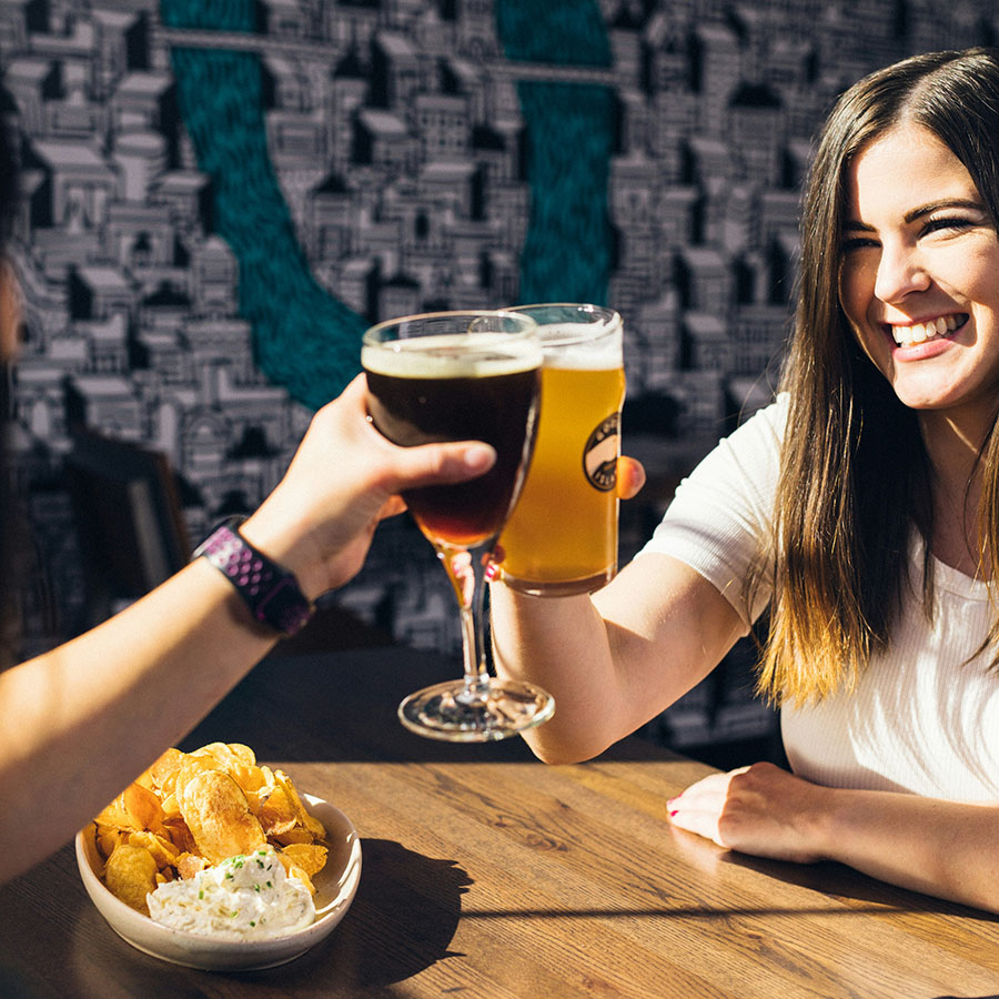 Friends toasting with beers at table with chips and salsa.