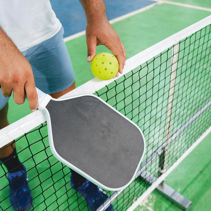 Person with pickle ball paddle and ball on outdoor court.