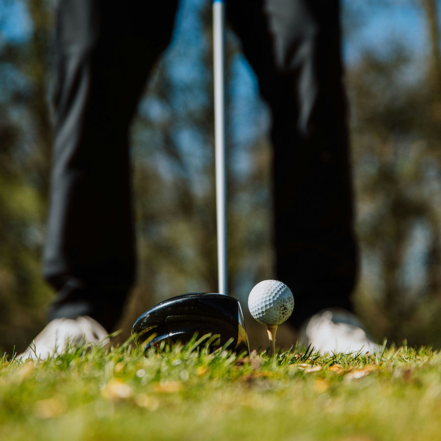 Person lining up a golf drive on grassy course.
