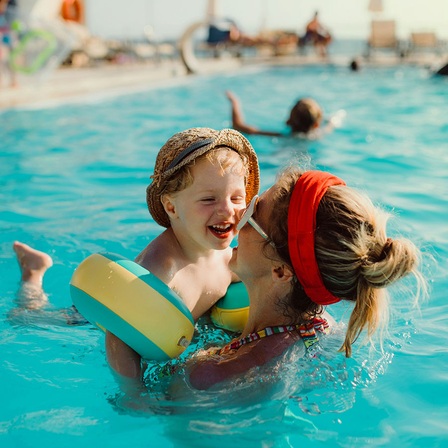Parent and child playing together in sparkling blue swimming pool.
