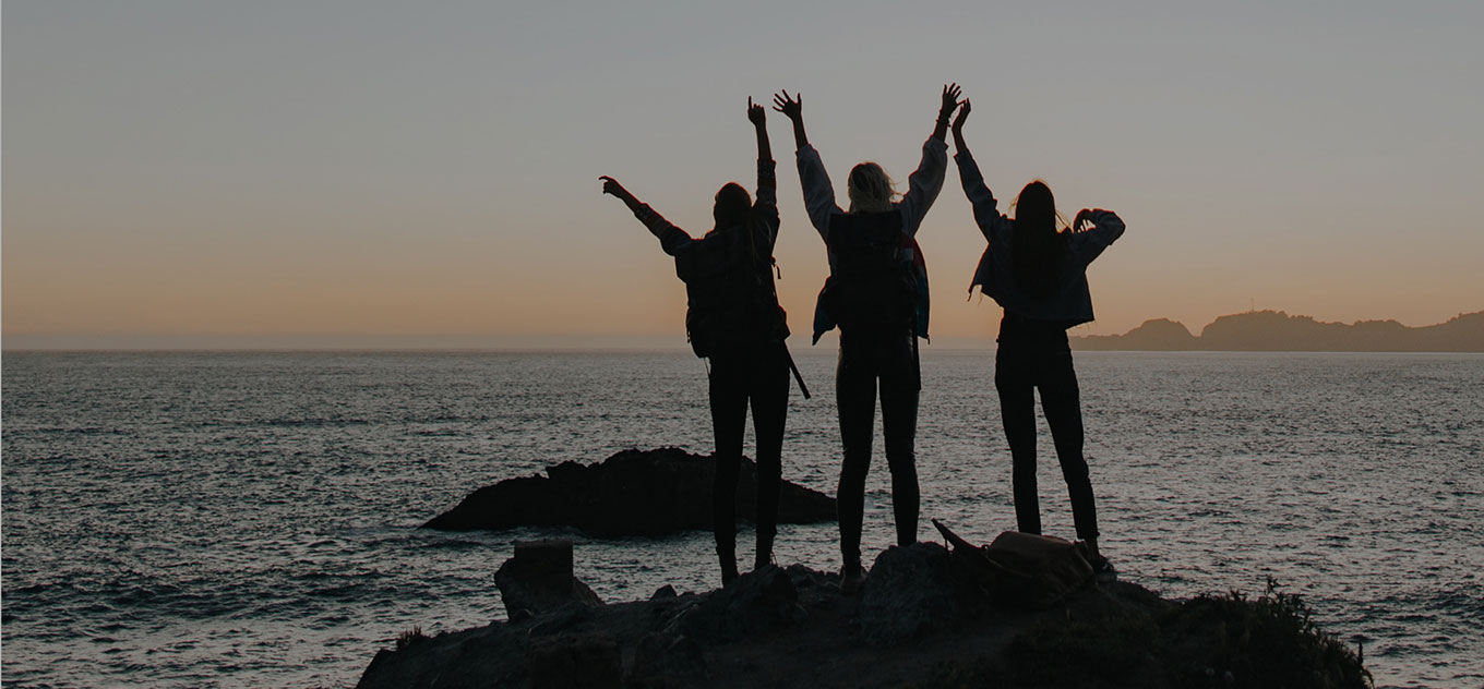 Friends waving together on rocky coastline.