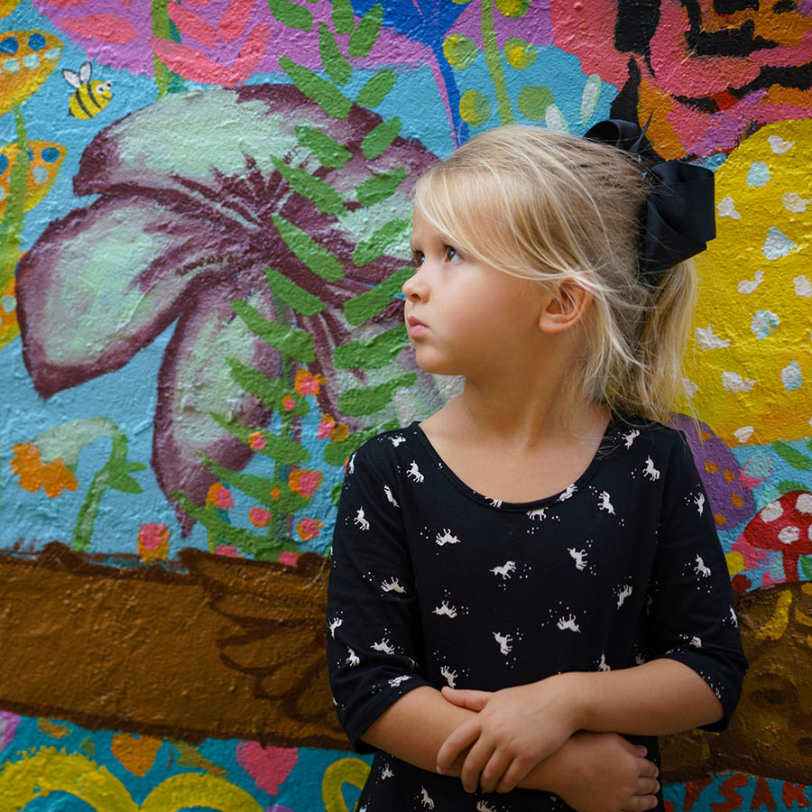 Child standing next to wall mural with colorful painted flowers.