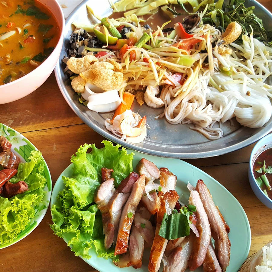 Plates of colorful fresh Thai food on wood table.