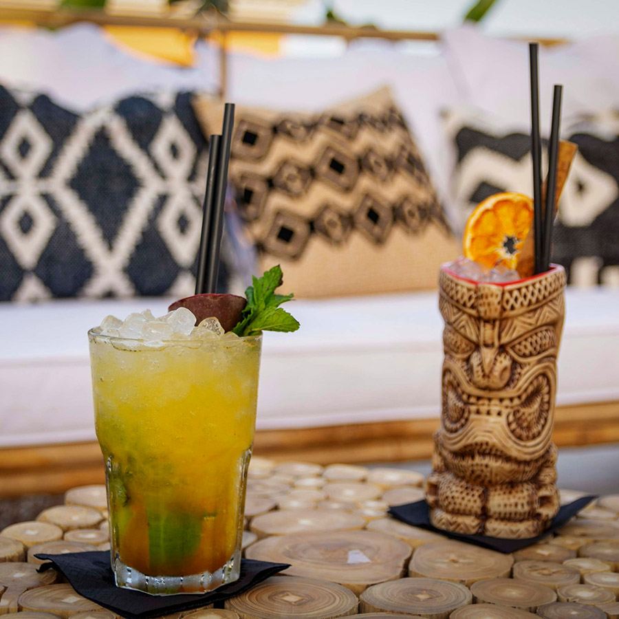 Two tropical cocktails in tiki mugs on table.