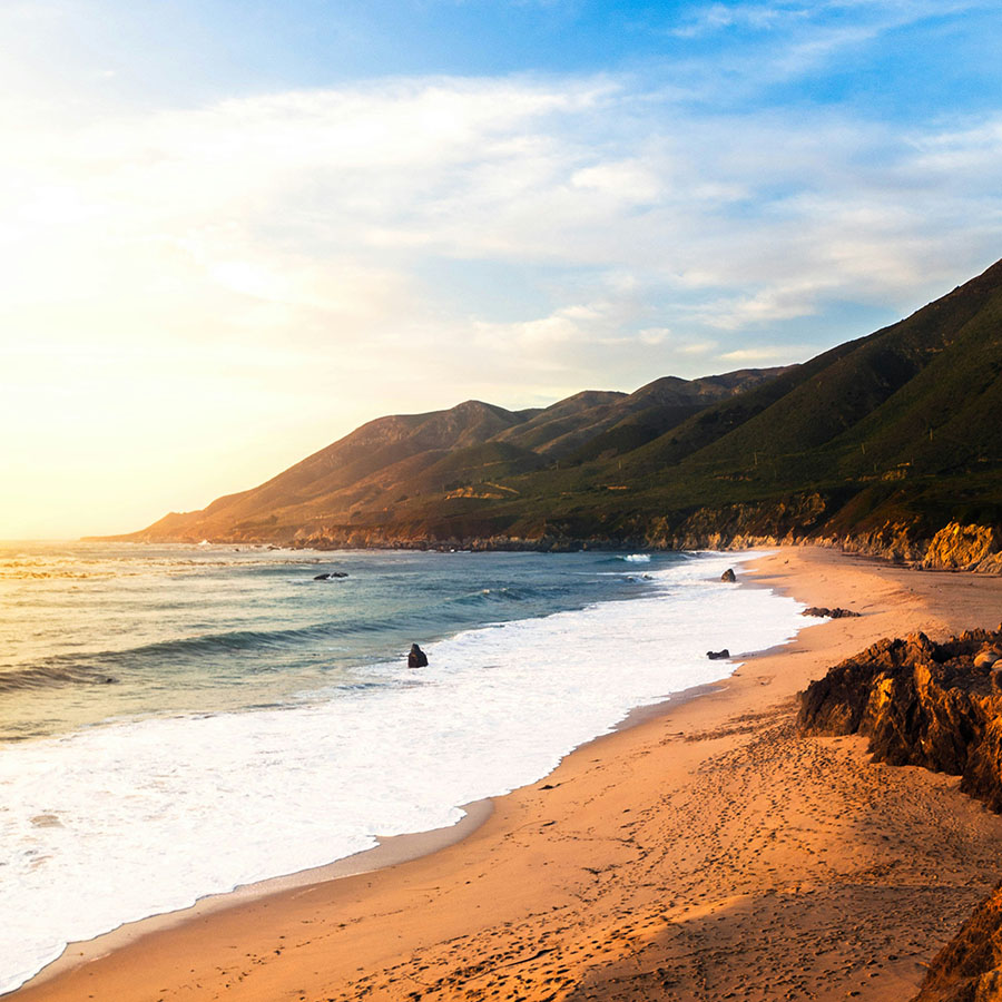 Stunning coastal beach with white waves and tall foothills.