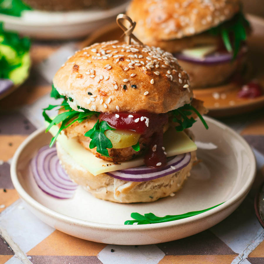 Large burger on round plate on colorful patterned table.