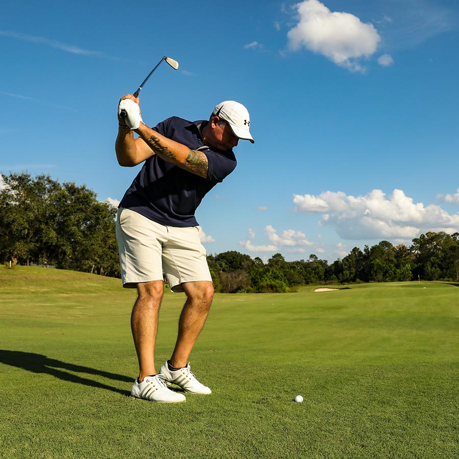 Person swinging golf club under cloudy blue skies.