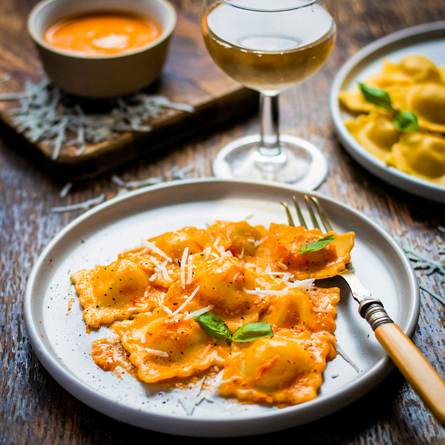 Plates of colorful pasta and wine glasses on elegant dining table.