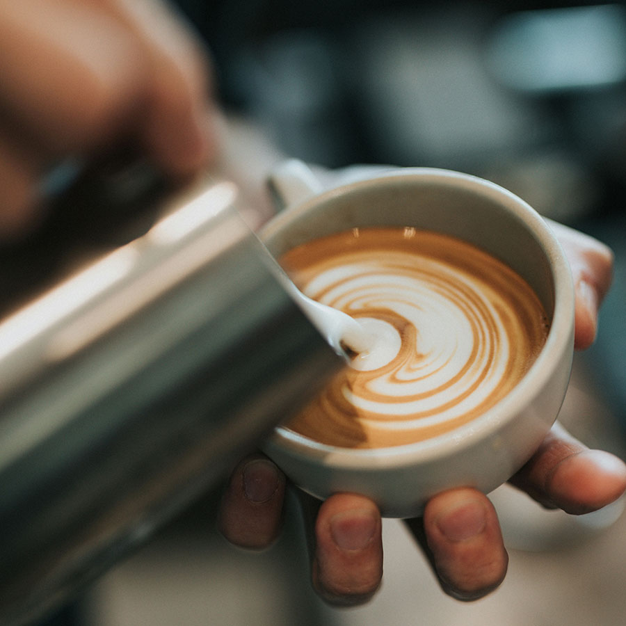 Person pouring latte foam art in cafe.