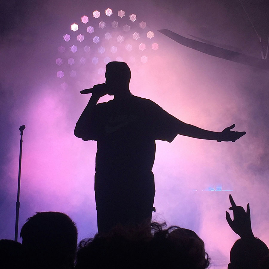 Musical performer at concert in front of fog and purple lights.