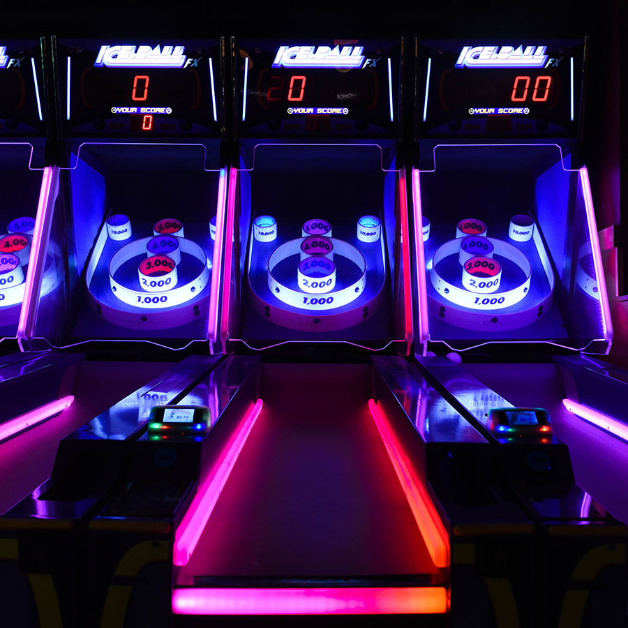 Skee ball machines with bright neon lights in dark arcade.