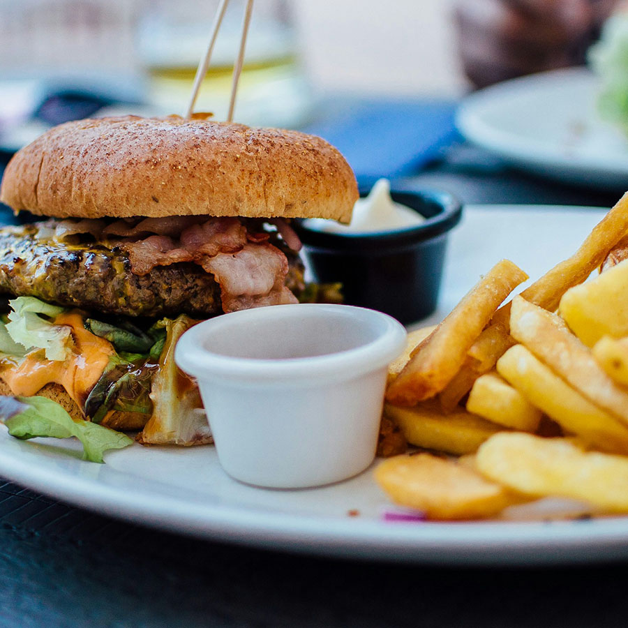 Plate with large bacon cheeseburger and pile of french fries.