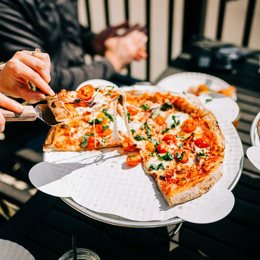 People at outside dining table sharing bright and fresh pizza.