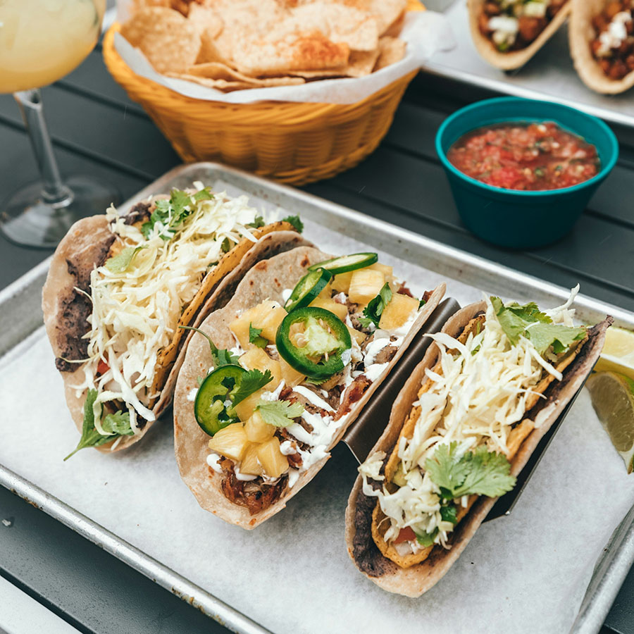 Tray of street tacos next to chips & salsa and margarita.