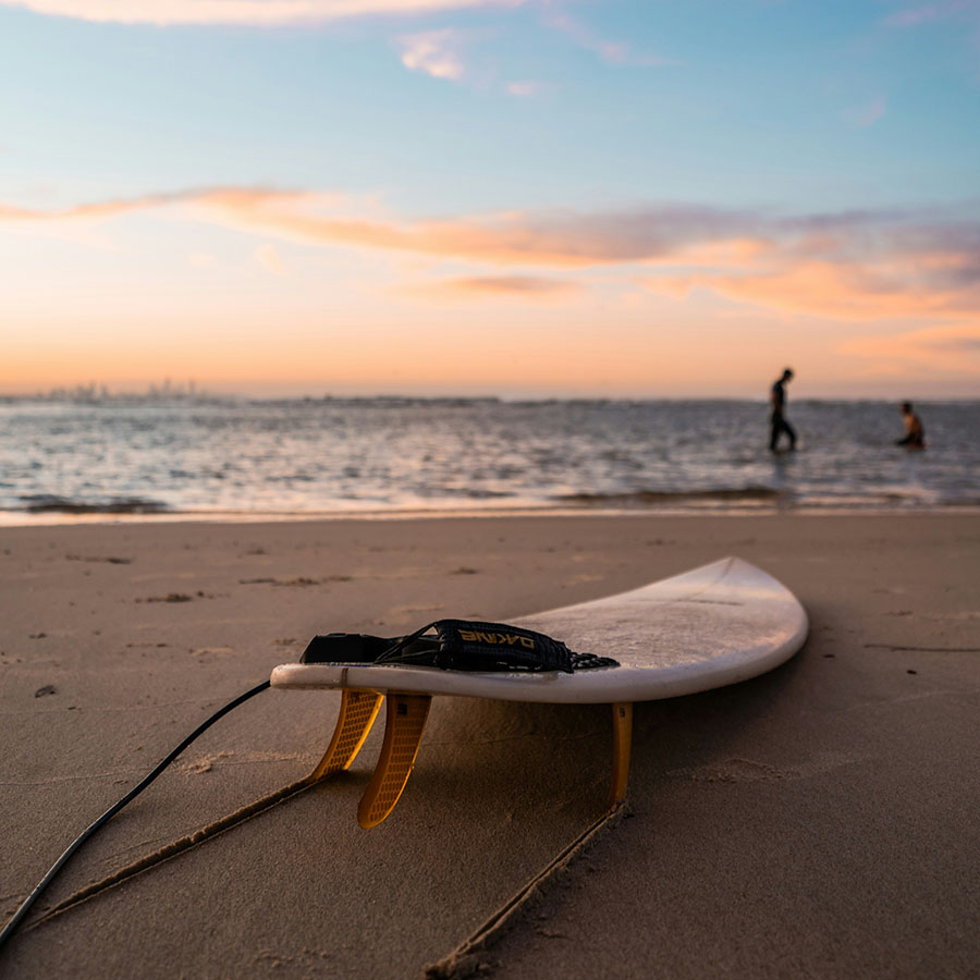 Surf board sitting on sandy coastal beach at sunset.