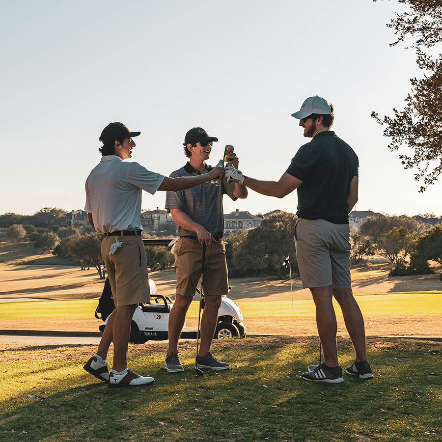 Friends toasting with drinks while playing golf outside.