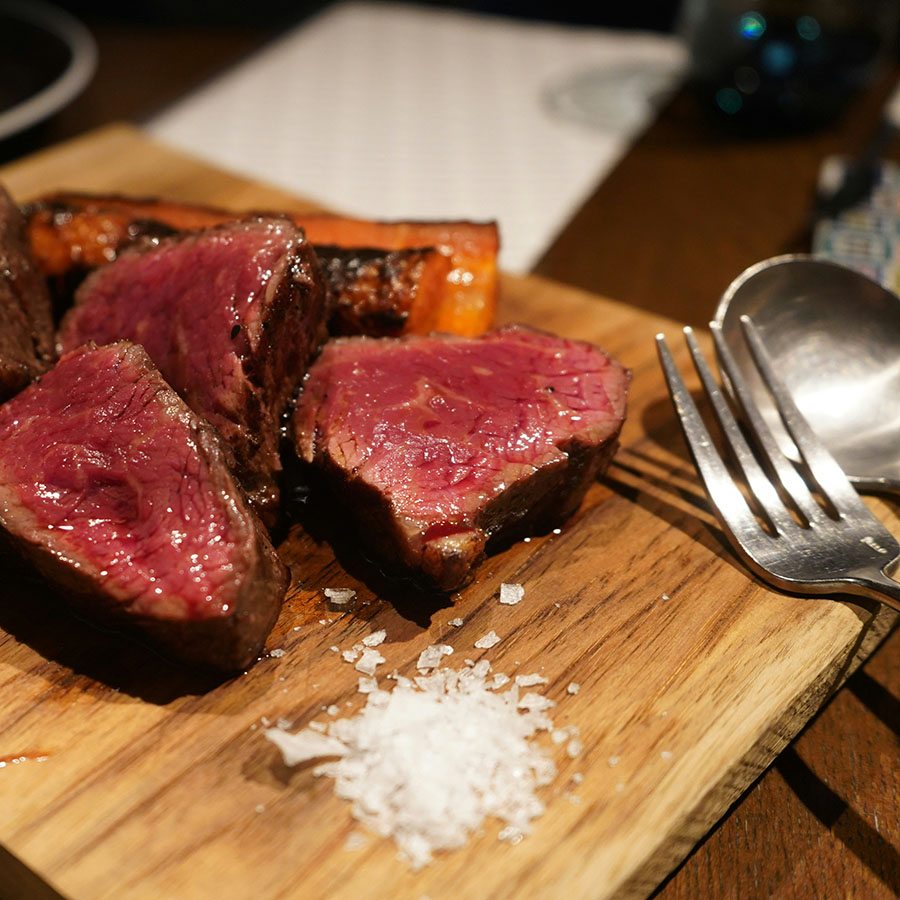 Sliced, rare steak on platter with a pile of coarse sea salt.