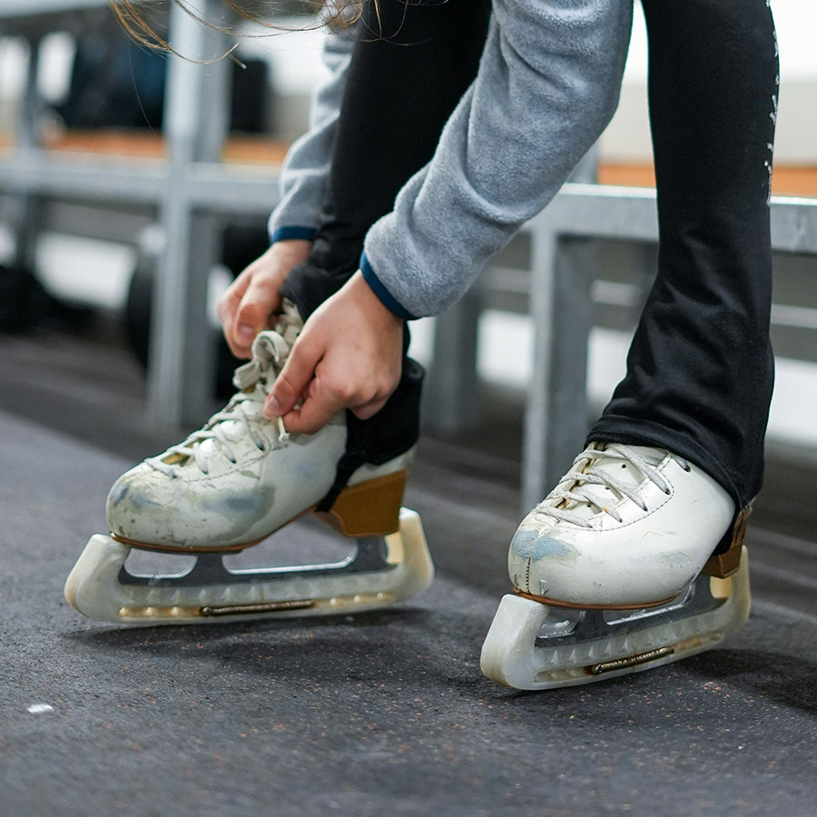 Person lacing up ice skates at skating rink.