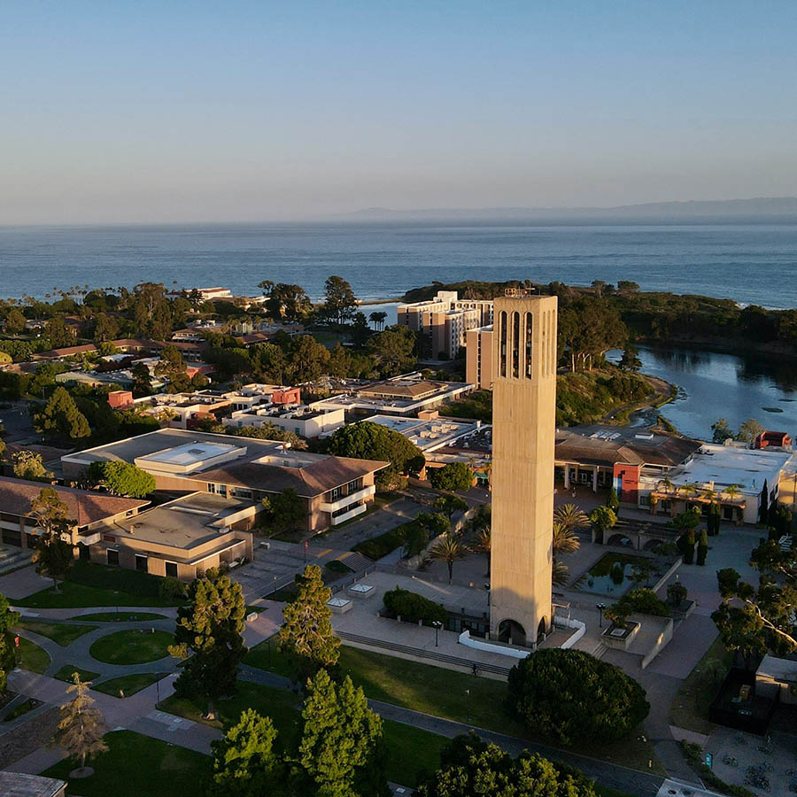 Aerial view of coastal town with tall tower and distant clouds.